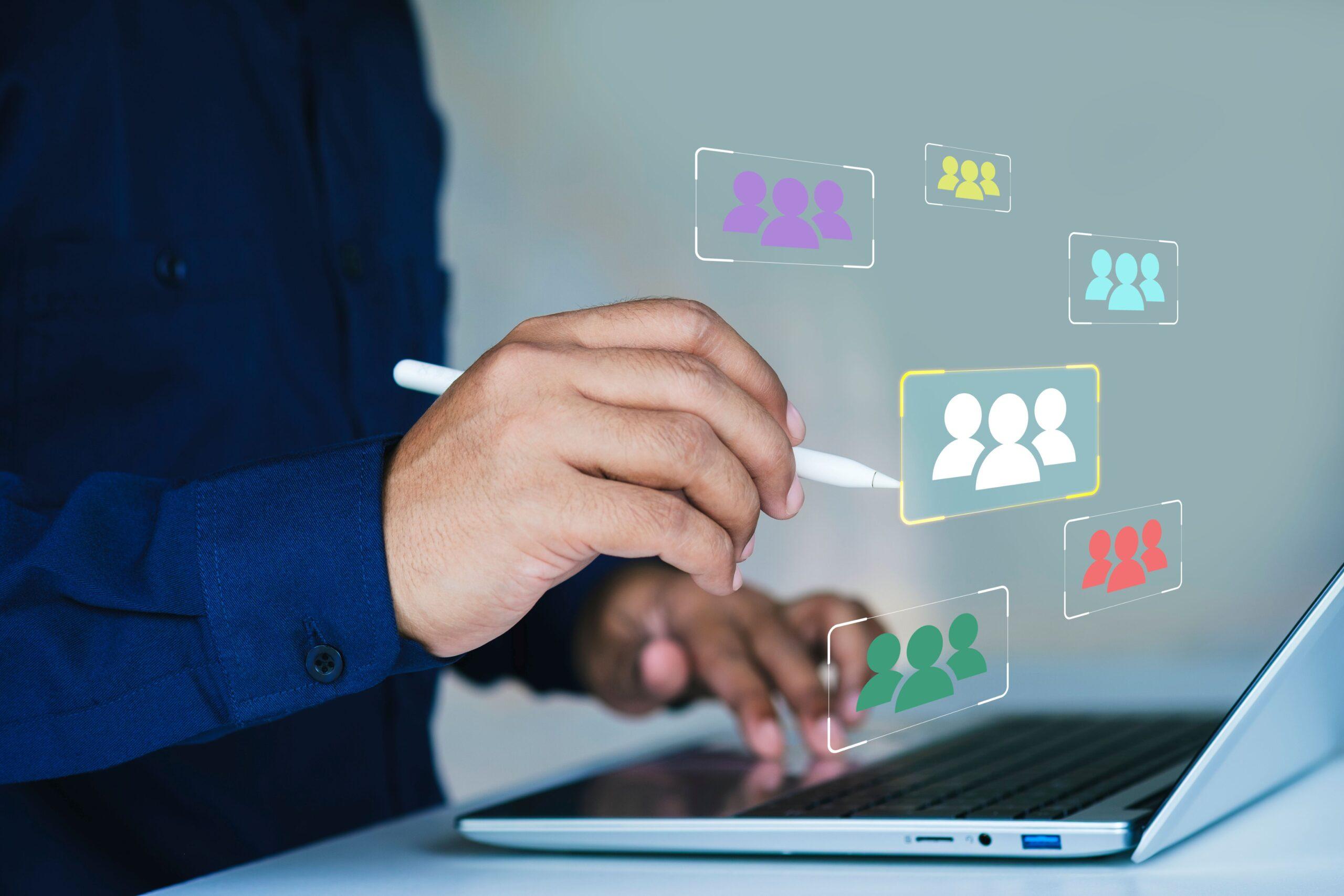 Close-up of a hand using a stylus on a laptop, selecting user group icons – representing task delegation in digital content management