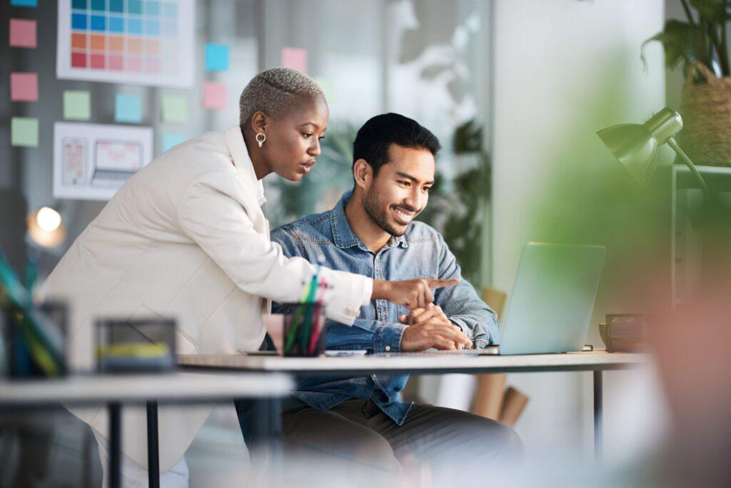 Two professionals working together on a laptop in a creative office, symbolizing the role of OnlyFans Managers in delegation and digital support for content creators